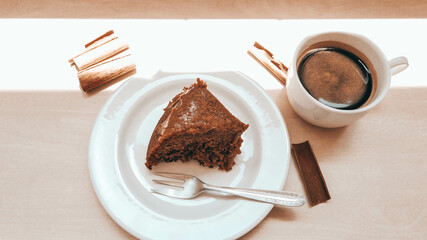 Slice of a cinnamon cake on a white plate next to a cup of coffee and sunlight reflection