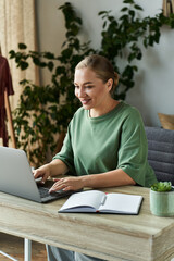 A cheerful plus size woman engages in her work at home, surrounded by plants and cozy decor.