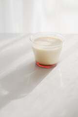 homemade Japanese caramel custard pudding in a glass cup on white  table in morning sunlight.