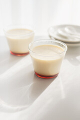 homemade Japanese caramel custard pudding in a glass cup on white  table in morning sunlight.