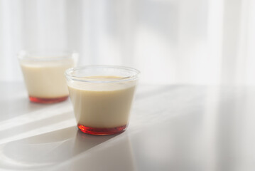 homemade Japanese caramel custard pudding in a glass cup on white  table in morning sunlight.