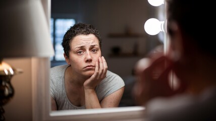 
woman holding her face and looking at herself in the mirror