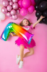 Joyful little girl lies on a pink background with balloons