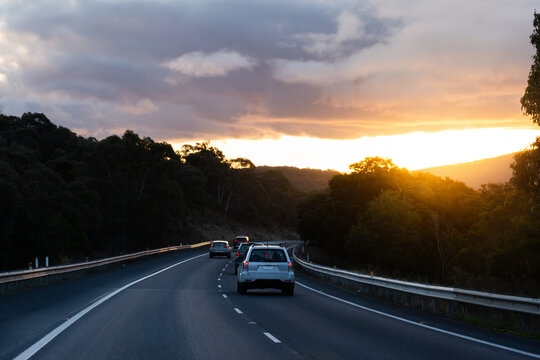 Golden sunset haze in sky above dark road late in the day as cars travel on rural highway
