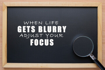A black chalkboard with motivational quote on life, "When Life Gets Blurry, Adjust Your Focus". A magnifying glass was placed at the edge of the chalkboard