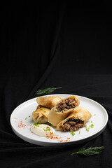Stuffed Crepes with Mushroom Filling and Sour Cream on a White Plate.