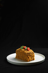 Slice of Honey Cake with Strawberries and Mint on a White Plate against Dark Background.