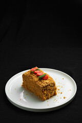 Slice of Honey Cake with Strawberries and Mint on a White Plate against Dark Background.