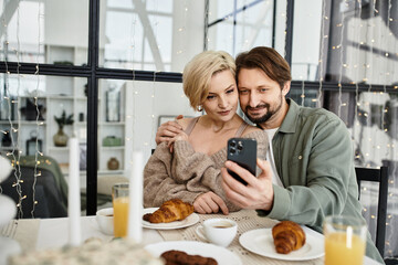 The couple sits at a table filled with breakfast treats, sharing joyful moments and laughs.