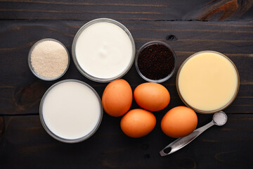 Coffee Creme Brulee Ingredients on a Wooden Table: Overhead view of eggs, coffee grounds, sweetened condensed milk, and more on a rustic background