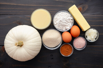 White Pumpkin Pie Ingredients on a Wooden Table: White pie pumpkin with flour, sugar, pumpkin spice, and other pumpkin pie ingredients