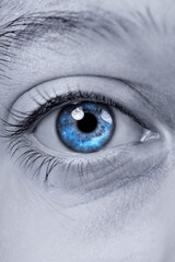 closeup of a blue eye set against a white background. The center of the eye is blue with glowing blue galaxy and stars and nebula. Macro close-up of a blue human eye looking straightforward.  
