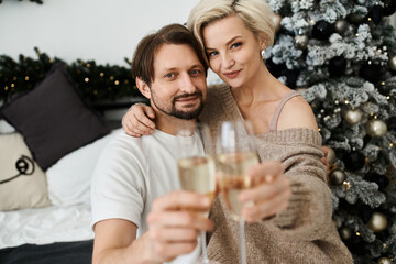 A joyful couple holds glasses of champagne, sharing a moment of love and warmth at home.