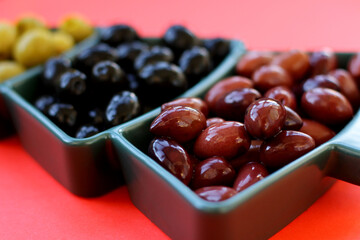 Green, black and red olives in a vase in the shape of a Christmas tree on a red background