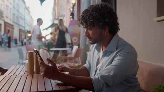 Indian Arabian man guy male student businessman tourist travel in cafe drink coffee outdoors city travel abroad using mobile phone gadget addict online buying shopping booking tickets trip vacation