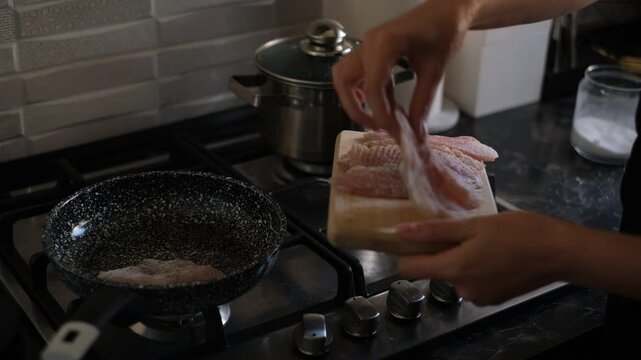 a young woman frying tilapia fish in a frying pan in her kitchen