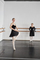 Vertical shot of slender teenage girl wearing black leotard spinning in graceful pirouette while practicing ballet moves in dance studio with white painted walls, copy space