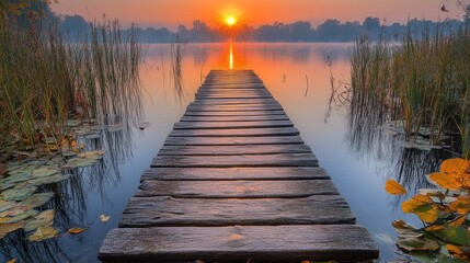 Obraz premium Wooden dock leading towards a sunrise over a misty lake.