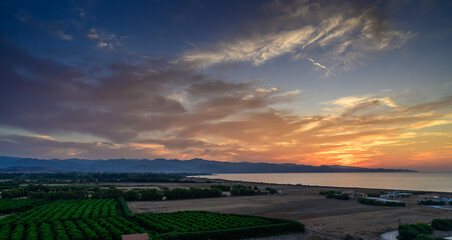 Vibrant sunset over lush orchards and a tranquil coastline near the mountains