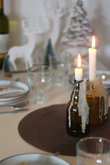 Table set for Christmas meal with plates, glasses, holiday decorations, lit candles and wine. Selective focus.
