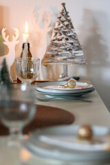 Table set for Christmas meal with plates, glasses, holiday decorations, lit candles and wine. Selective focus.