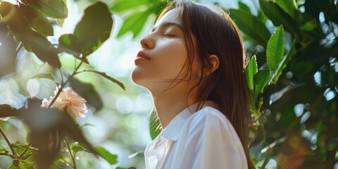Young woman appreciating the fragrance of a blooming flower in a forest setting.