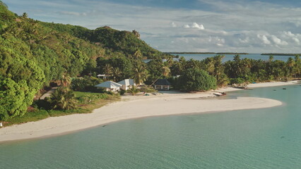 Aerial flight over bungalows houses on private small beach. Crystal water, white sand, palm trees, green hill landscape. Remote wild nature tropical island paradise, exotic vacation summer travel