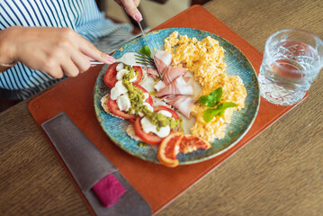 Woman having delicious breakfast with scrambled eggs and bruschetta in restaurant
