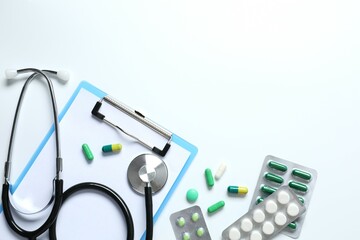 Stethoscope with pills and clipboard on color background, top view