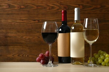Two bottles of red and white wine with glasses and grapes on wooden table