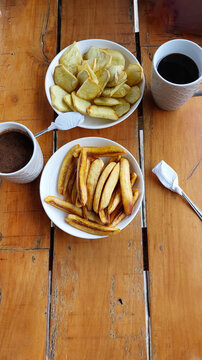 Rustic wooden table setting with mugs of coffee, bowls of pritong saging or fried banana and sweet potatoes or kamote for a traditional Filipino afternoon snack