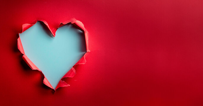 Ripped paper hole heart shaped on red paper background. Valentine`s day celebration concept.