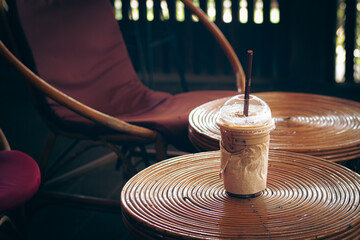 Iced coffee on a round rattan table next to a rattan chair in a cozy dimly lit cafe