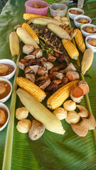 Traditional Filipino boodle fight or sharing meal with grilled fish, corn, bananas, and various rice cakes served on banana leaves showing the authentic food culture of the Philippines