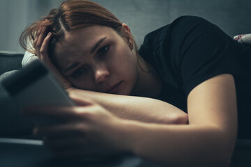 The girl is procrastinating: lying with a phone in her hands, a lazy expression on her face, a concentrated look