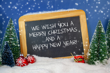 Christmas decoration with miniature trees and slate plate with we wish you a merry christmas and a happy new year with some falling snow flakes