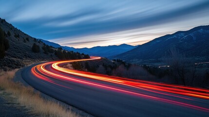 A winding mountain road at dusk with streaks of red taillights from cars driving by.