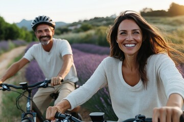 Obraz premium A smiling couple cycles through lavender fields during sunset, surrounded by mountains, representing freedom, joy, and connection with nature in a picturesque scene.
