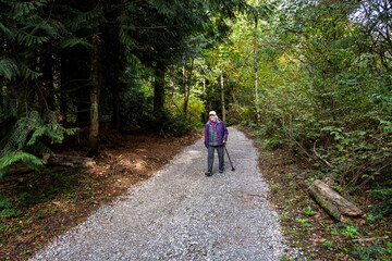 Obraz premium Senior woman with a walking stick getting fresh air on a gravel trail on a sunny fall day in the woods in Kirkland’s Watershed Park 