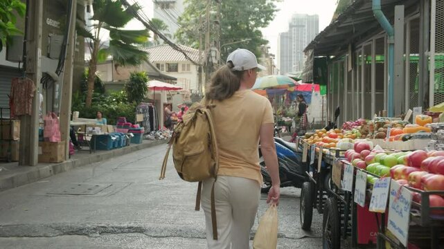 Woman walks through street market with fruit and vegetable stalls 