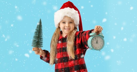 Cute little girl in Santa hat holding alarm clock and toy fir tree on blue background. Christmas countdown concept