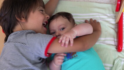 Young boy lying beside his baby sibling, smiling and enjoying a playful and joyful moment together in a warm family setting