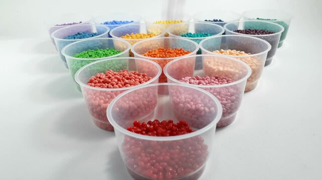 Red masterbatch granules are poured into a cup among various other colors. Color pigment carrier polymers in the plastics industry