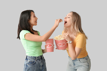 Beautiful young women with buckets of popcorn on white background