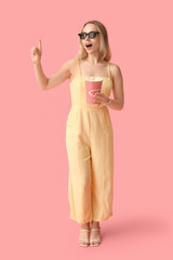 Young woman in 3D glasses with bucket of popcorn on pink background