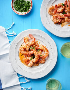 Garlic and chilli prawns served on white plates on a blue background