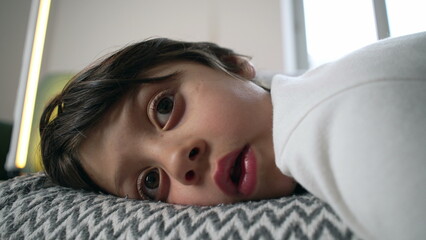 Young boy resting on a couch, close-up of his face as he watches a cartoon off-camera in a calm, reflective indoor setting