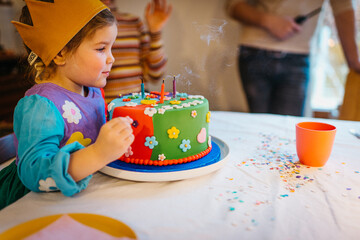 Cute girl Blowing Birthday Candles On Colorful Cake In Party Setting