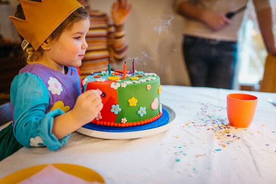 Cute girl Blowing Birthday Candles On Colorful Cake In Party Setting