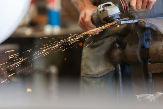 closeup Senior artist operating a grinder, sparks flying from th